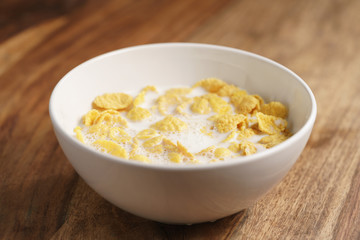 corn flakes with milk in white bowl on wood table, simple healthy breakfast