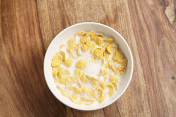 corn flakes with milk in white bowl on wood table directly above, simple healthy breakfast