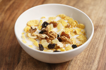 corn flakes with fruits and nuts in white bowl on wood table, simple healthy breakfast