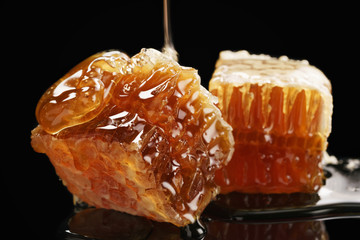 two pieces of organic honeycomb with honey isolated on black background with reflection