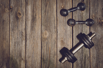 Old iron dumbbells or exercise weights outdoor on an old wooden deck, floor or table in the gym. Image frame taken from above, top view. A lot of copy space around product