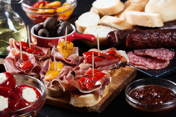 Spanish tapas with slices jamon serrano and grilled pepper. Also olives, salami, pickled onions, and peppers stuffed with cheese