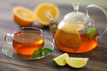 Glass teapot and cup of black tea with orange, lemon, lime  mint on a wooden table