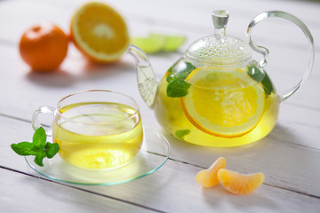 Glass teapot and Cup with green tea, orange, Mandarin, lime  mint on white wooden table