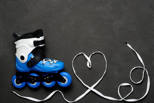 Blue roller skates and heart from laces on dark chalk board background