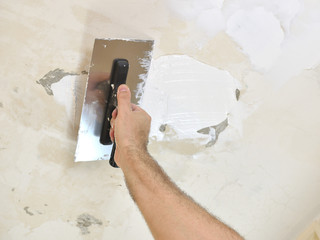 Troweling spackle on ceiling with finishing trowel