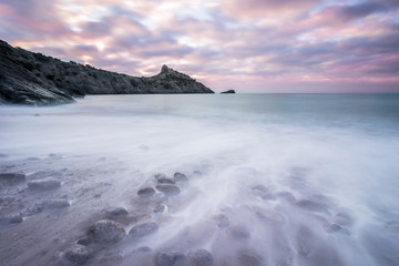 Fototapeta na wymiar Seascape at sunrise. stones, sea waves, rocks and long cape. Cloudy sky.