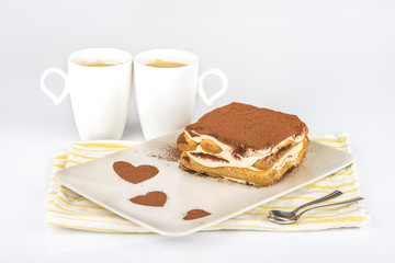 Tiramisu /
Tiramisu cake in a plate with a cocoa decoration and two cups of coffee on a white background
