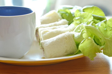 roll bread filled bologna and green oak with coffee cup on plate