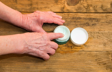 Old woman applying hand cream at home. Close-up of wrinkled woma