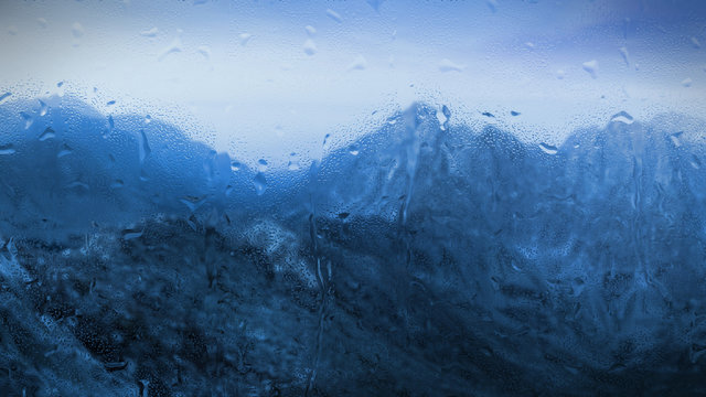 Fototapeta raindrops on a window with bluish mountainous landscape outside