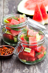 Marinated  watermelon with herbs in a glass jar on wooden table