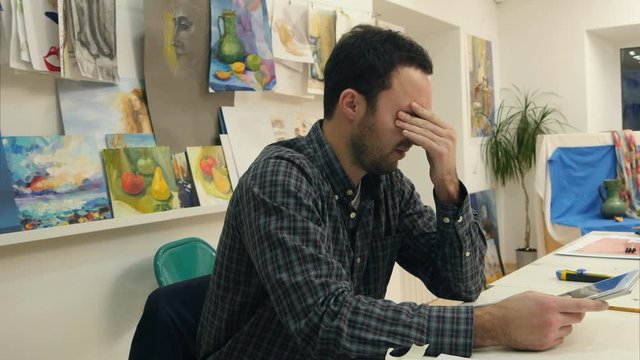 Tired and sleepy art teacher holding tablet at his desk