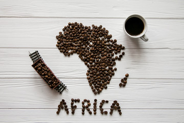 Map of the Africa made of roasted coffee beans and toy train and cup of coffee on white wooden textured background with space for text