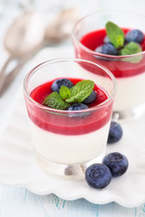 Delicious Italian dessert Panna Cotta for two with fresh blueberries and raspberry coulis in small transparent glasses for Valentine’s day