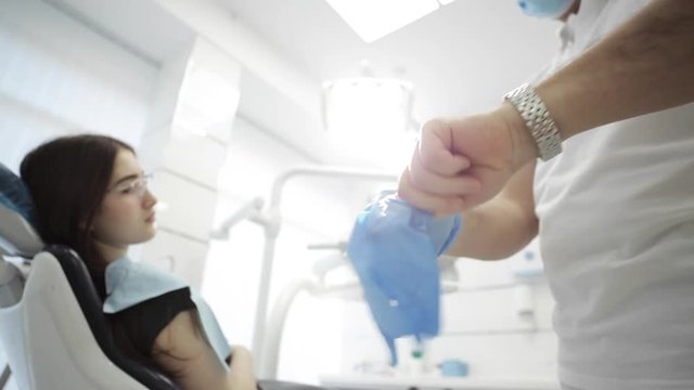 Male dentist putting on his gloves with patient on the background