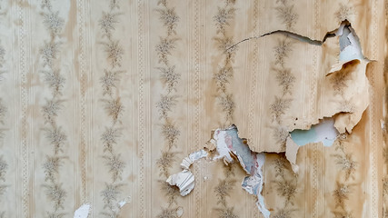 Fragment of old destroyed wall with jagged torn vintage wallpape