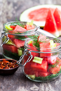 Marinated  watermelon with herbs in a glass jar on wooden table