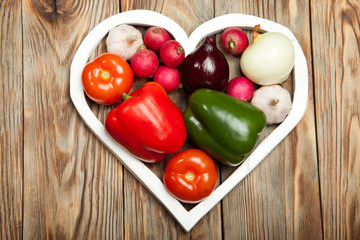 Vegetables. Peppers, tomatoes, garlic, onions, and radishes in the heart on rustic background