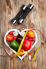 Sport and diet. Vegetables, dumbbells  centimeter. Peppers, tomatoes, garlic, onions,  radishes in the heart on rustic background