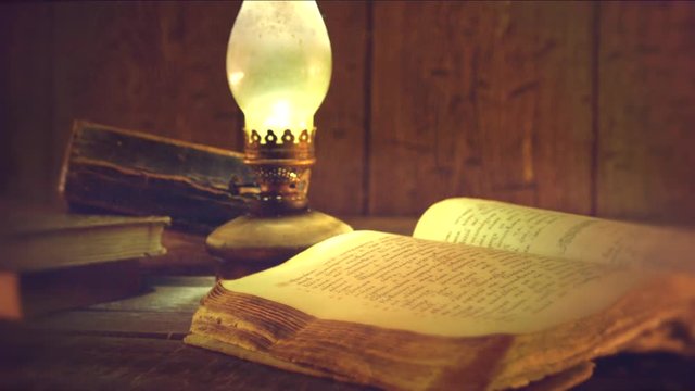 Old books and vintage oil lamp. Kerosene lantern and open old book on wooden table. 4K UHD video footage. Ultra high definition 3840X2160