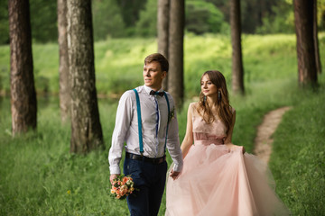 Wedding couple, beautiful bride in peach dress and groom with bow tie and suspenders walking in...