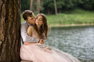 Happy wedding day, groom kisses bride on cheek near river with copy space. Wedding love