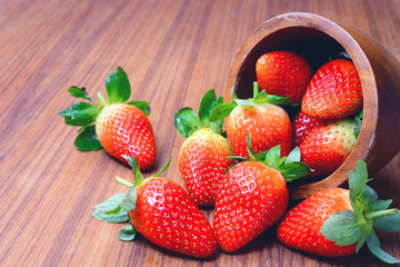 Fresh strawberries in a bowl decorated by cut strawberry on rustic wooden table.