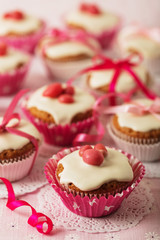 Cupcakes with white icing decorated with pink candy and ribbons.