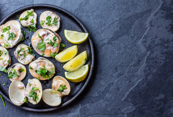 Raw clams with lemon, herbs and white wine, slate background