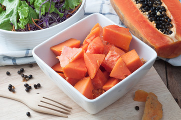 kitchen table with sliced fresh papaya fruit on wood cutting board and vegetable salad, nutrition...