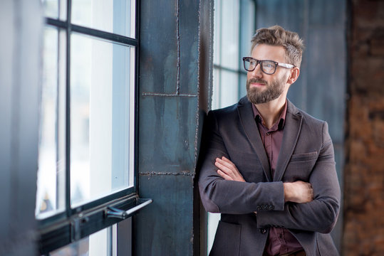 Portrait of caucasian bearded businessman dressed in suit with eyeglasses near window in the loft interior office