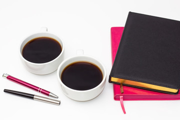 two of the diary, two cups of black coffee and two pens on a white background. flat lay of the business concept of relationship men and women