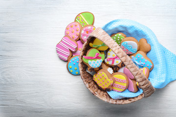 Wicker basket with tasty Easter cookies on white wooden background