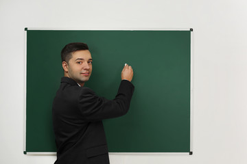 Handsome young teacher writing on blackboard in classroom