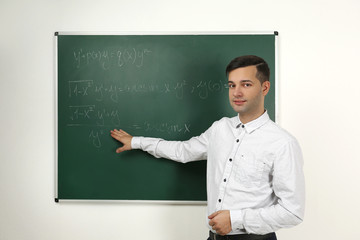 Handsome young teacher explaining math formulas written on blackboard