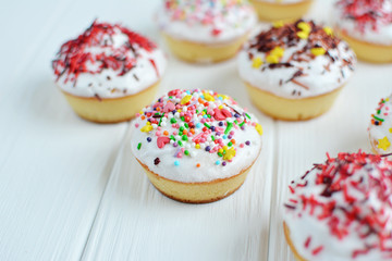 Fototapeta na wymiar Cupcakes with white cream and sprinkles on white background