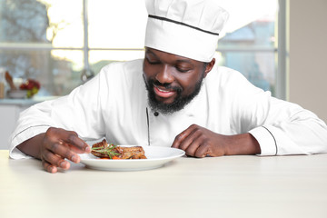 African American chef cooking tasty meat in kitchen