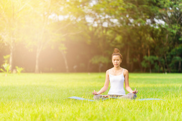Asian girl do yoga meditation at the park in the morning with sunlight