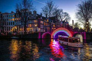 AMSTERDAM, NETHERLANDS - JANUARY 10, 2017: Cruise boats rush in night canals. Light installations...