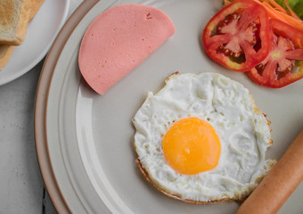 Eggs and ham sausage with tomato on white plate.