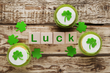 Green paper clover leafs and tasty cupcakes on a grey wooden tab