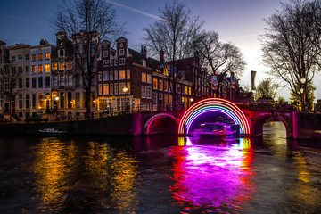 AMSTERDAM, NETHERLANDS - JANUARY 10, 2017: Cruise boats rush in night canals. Light installations...