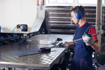 Inside a factory, industrial worker in action on metal press machine holding a steel piece ready to be worked.