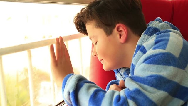 Portrait of a child little boy with winter clothes  sitting by the window  looking at the winter view