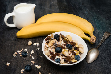 Delicious and healthy muesli in bowl with milk and bananas on dark wooden  table