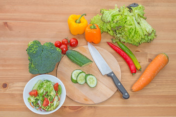 Chopped salad and whole fresh vegetables on wooden table. Top view.