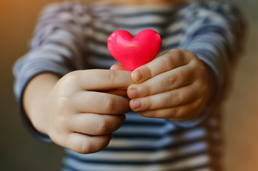 child holding a small pink heart. symbol of love, family, hope. Backgrounds for cards on Valentine's Day. Backgrounds for social posters about the preservation of the family and children. - obrazy, fototapety, plakaty