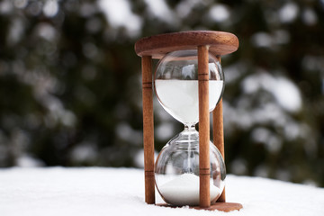 hourglass in the snow, white sandglass time passing in a winter landscape 