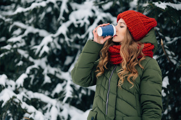 Winter coffee outdoors. Woman in warm winter clothes drinks coffee outdoors in winter snowy day. Woman with coffee